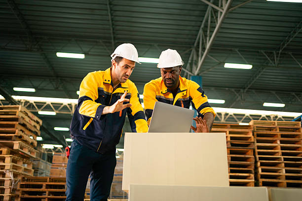 istock Two Warehouse Workers in hard hats review inventory data on a laptop amid stacked pallets and shelving in a modern distribution center. 2228647770