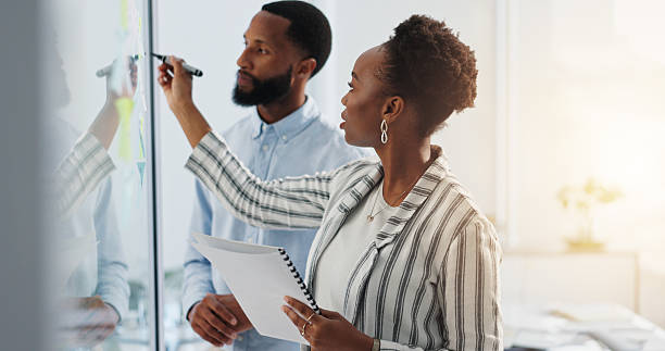 istock Business people, writing and schedule planning with glass board for reminder, project or tasks. Businessman, woman or colleagues with notes for team brainstorming, ideas or deadline in workplace 2228651948