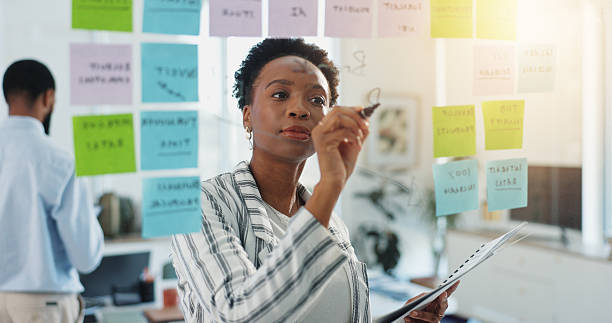 istock Business woman, writing or planning with glass board for reminder, project or schedule tasks. Female person, planner or agenda with notes or idea for event, calendar or office delegation in workplace 2228651950