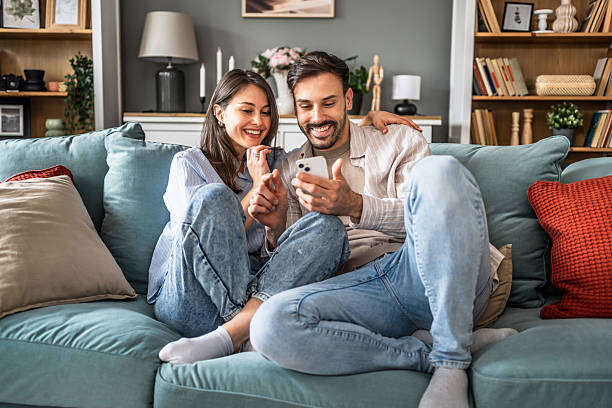 istock Young couple relaxing on sofa, browsing social media on smartphone 2228653760