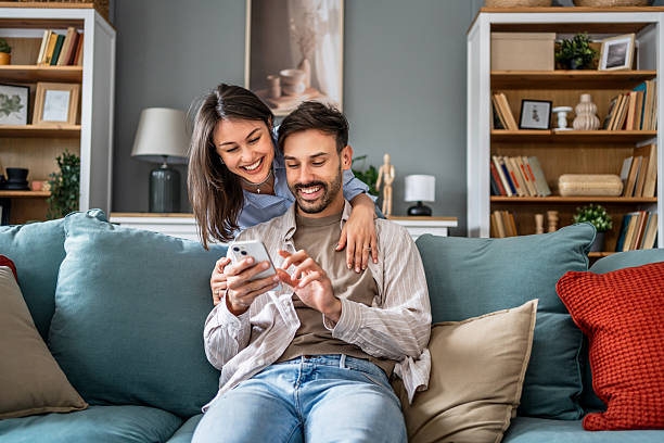 istock Young couple relaxing on sofa, browsing smartphone together at home 2228654180