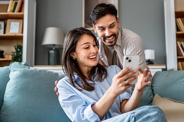 istock Young couple relaxing on sofa, browsing social media on smartphone 2228654480