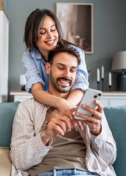 istock Young couple relaxing on sofa, browsing smartphone together 2228654590