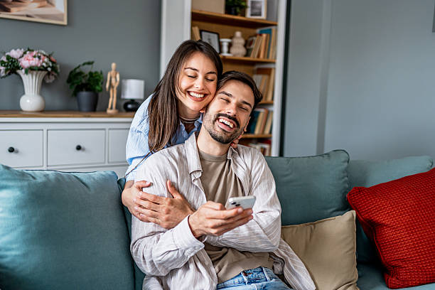 istock Young couple relaxing on sofa, embracing and using smartphone at home 2228654630