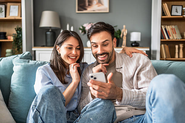istock Young couple relaxing on sofa, browsing social media on smartphone 2228654738