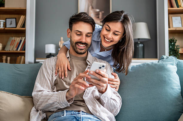 istock Young couple relaxing on sofa, browsing social media on smartphone 2228654847