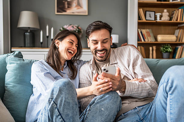 istock Young couple relaxing on sofa, enjoying funny content on smartphone 2228654945