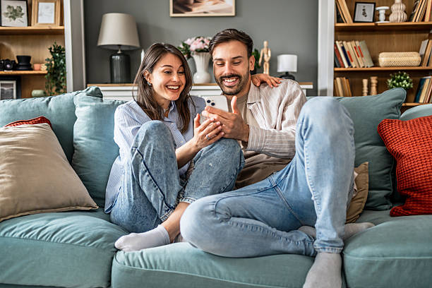 istock Young couple relaxing on sofa, browsing social media on smartphone 2228654984