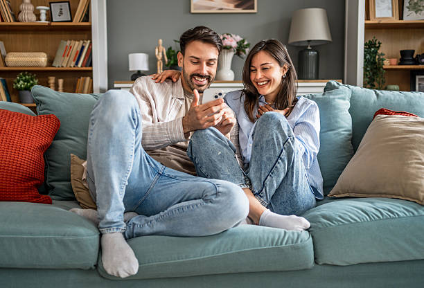 istock Young couple relaxing on sofa, enjoying funny content on smartphone 2228655093