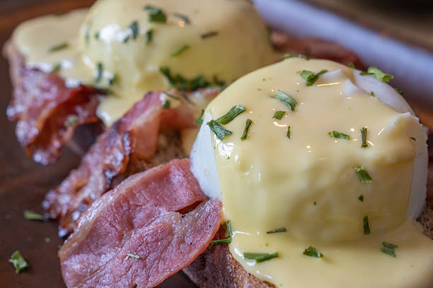 Close-up showing eggs benedict nestled on crispy toast, topped with sizzling bacon and sprinkled with freshly chopped chives