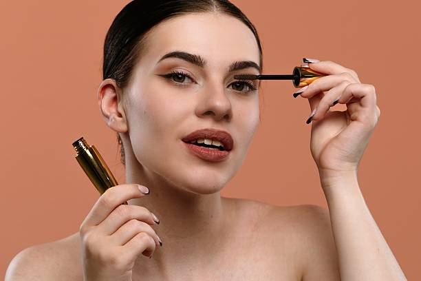 istock Woman Applying Mascara On Eyelashes With Orange Background 2228656412