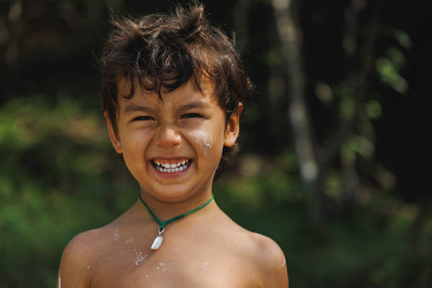 A young, happy child smiling brightly against a blurred natural background, exuding joy and energy. Perfect for depicting happiness, childhood innocence, and outdoor activities on a sunny day.