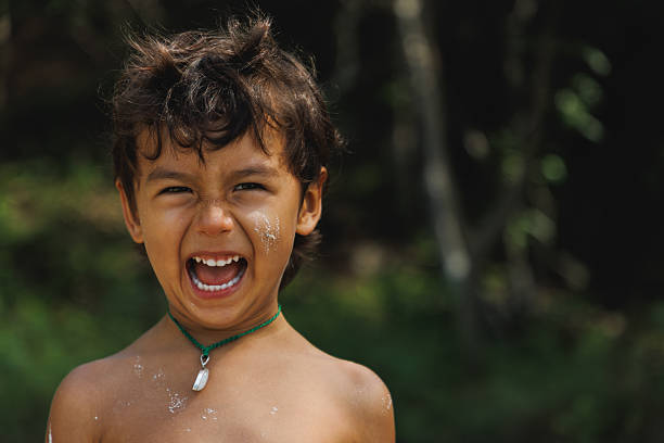 Energetic boy expressing happiness outdoors, sunlight illuminating the playful atmosphere amidst nature.