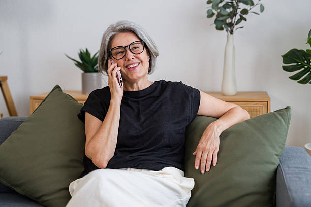 istock Smiling mature woman talking on smartphone while relaxing on sofa at home 2228658852