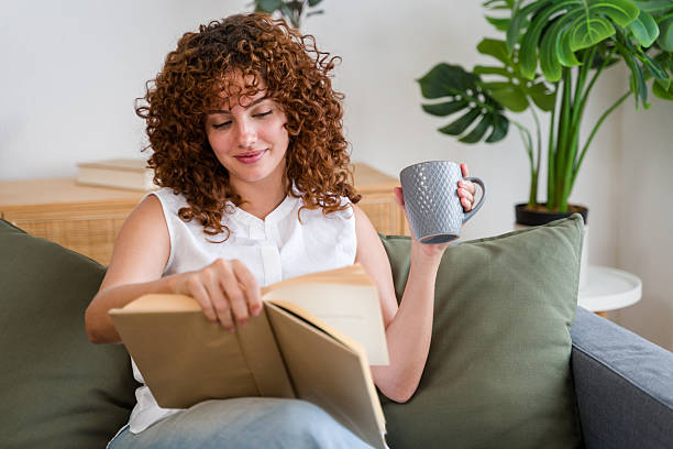 istock Young woman relaxing on sofa reading a book and drinking tea 2228659007