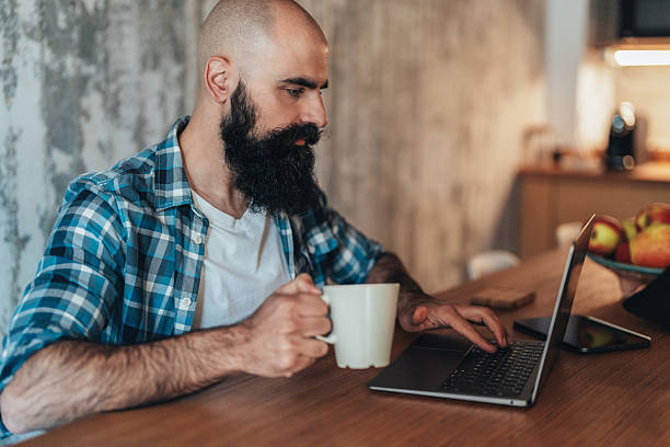 istock Serious man sitting at a wooden table working on a laptop 2228660272