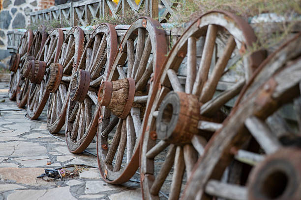 A rustic wooden wagon wheel leaning against a stone wall in a sunny outdoor setting.