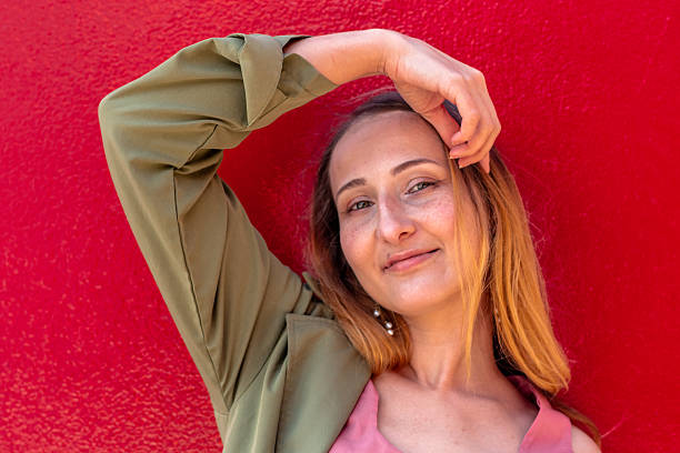 istock Stylish woman posing with hand on head against red wall 2228669327