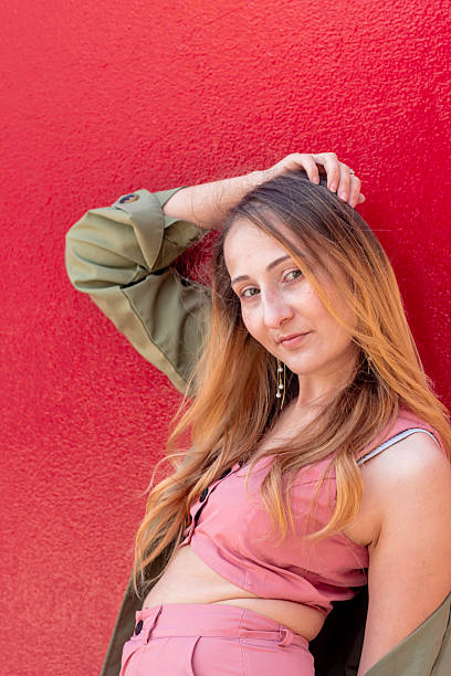 istock Young influencer posing with hand on hair against red wall 2228669536