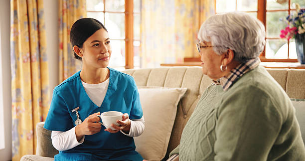 istock Caregiver, elderly woman and tea on sofa with discussion, support feedback and relax in retirement home. Assisted living, senior patient and nurse in lounge with drink, bonding and daily checkup 2228676739