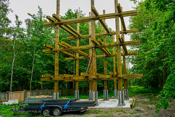A large wooden frame structure is being built for an outdoor entertainment obstacle course in a wooded area