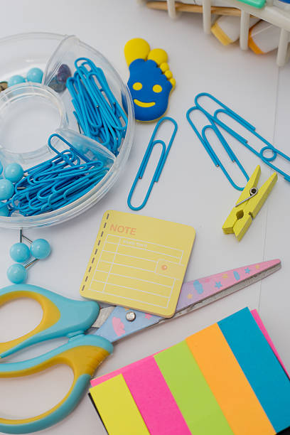 Bright school and office supplies including scissors, pens, pencils, sticky notes, paper clips, and markers scattered on a white surface.