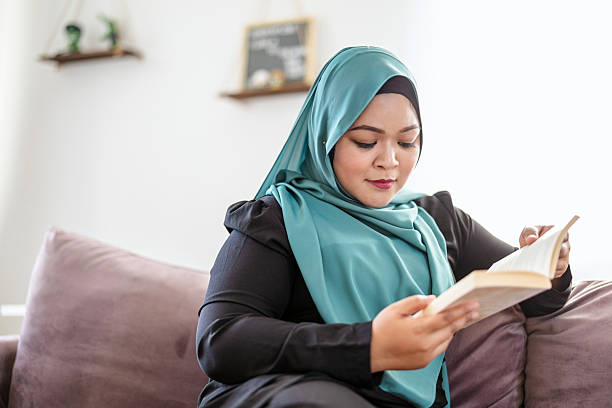istock Woman in hijab reading a book while sitting on a sofa in her home 2228691430