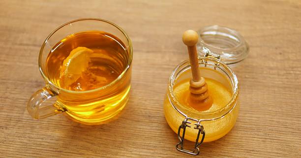 istock Transparent cup of aromatic tea with fresh lemon slice and honey jar on table 2228692552