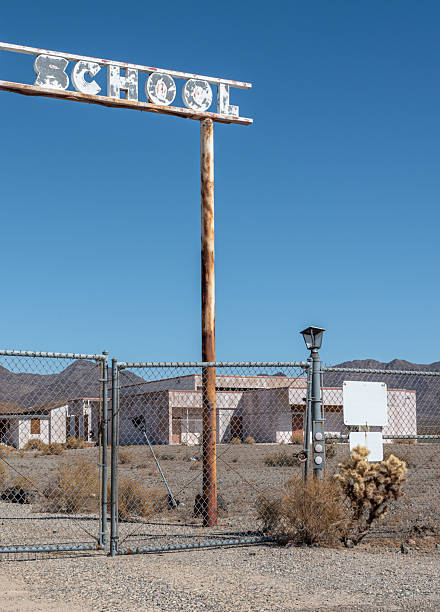 Sign at abandoned school in the Mojave Desert, with locked chain link fence and deteriorating buildings.