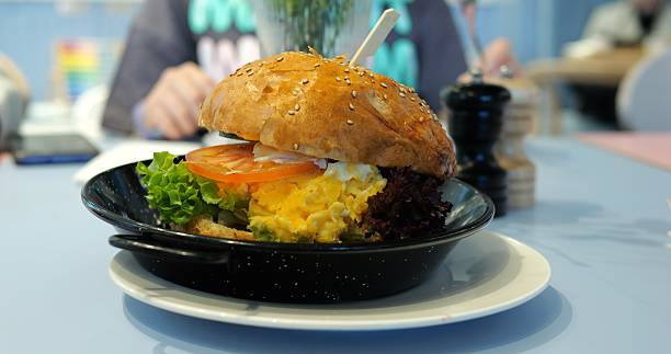 Burger features scrambled egg on table against visitor eating in restaurant