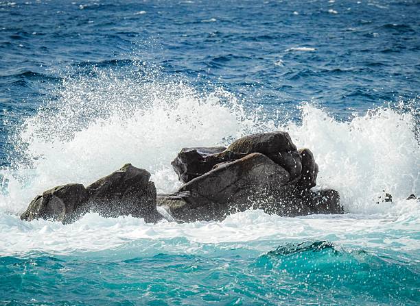 Waves crashing against rocks in the ocean with splashes and blue water creating a dynamic seascape.