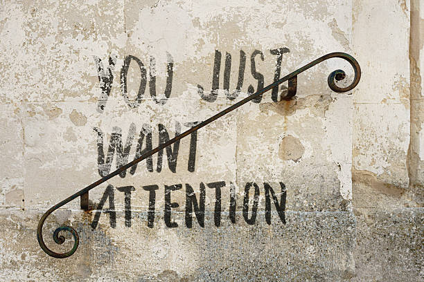 Black stencil graffiti reading YOU JUST WANT ATTENTION appears on a weathered, peeling plaster wall. A diagonal, rusted wrought-iron railing cuts across the text, creating a layered interplay between message and environment.\n\n***The text was digitally superimposed and a release is provided***