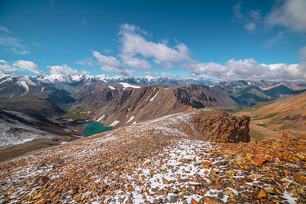 istock Two high mountain valleys separated by sharp rocky ridge. Freshly fallen snow on stony pass in sunlight. Most beautiful alpine lake. Large colorful mountain range with snow-white peaks in low clouds. 2228702128