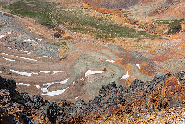 istock Scenic dizzy top-down view from precipice edge with sharp rocks to unusual multicolor stony valley with iron river in sunlight. Colorful awesome alpine scenery with snow in multi-color hilly valley. 2228702155
