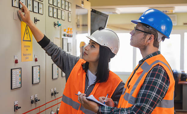 istock Young Female and Male Engineers Operating Electrical Control Panel in Modern Power Plant Control Room with Safety Helmets and High Visibility Vests 2228703235