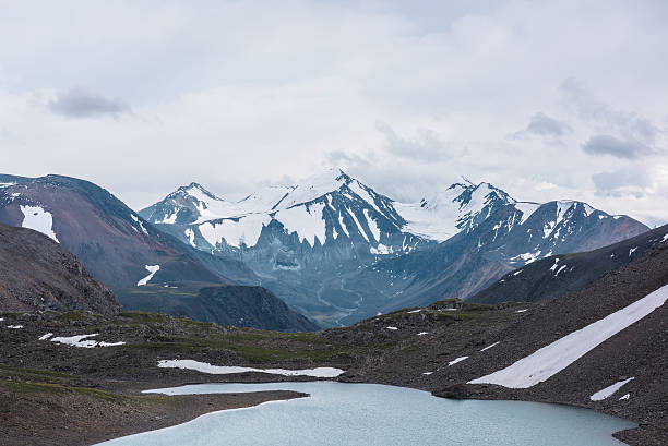 istock Dramatic view to most beautiful blue alpine lake against snow-covered range with few pointy peaks. Atmospheric landscape with azure mountain lake against three snowy peaked tops under gray cloudy sky. 2228708490