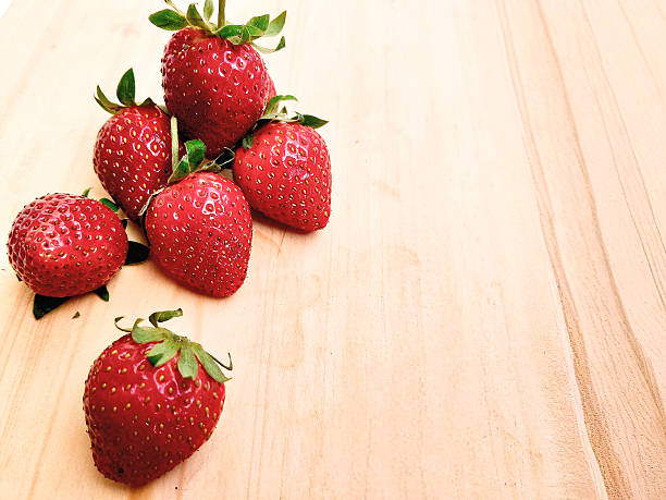 A vibrant pile of fresh organic strawberries on a rustic wooden cutting board, perfect for culinary themes, healthy lifestyle visuals, and seasonal food concepts.