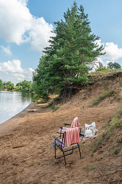 Folding chairs with towels, bags, a mat on a wild sandy beach.