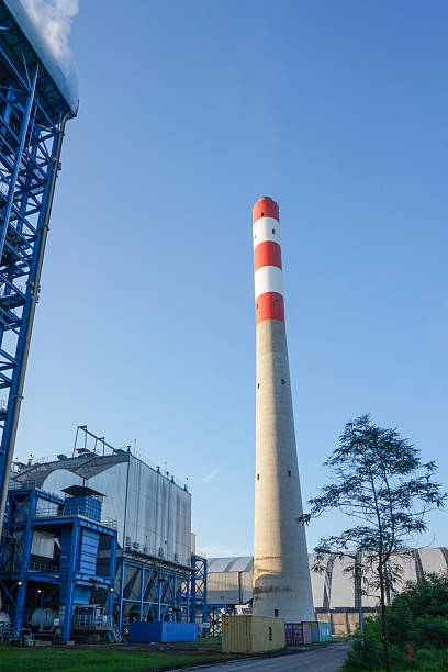 Industrial landscape featuring a tall smokestack against a vast blue sky emphasizing industrial scale and environmental themes
