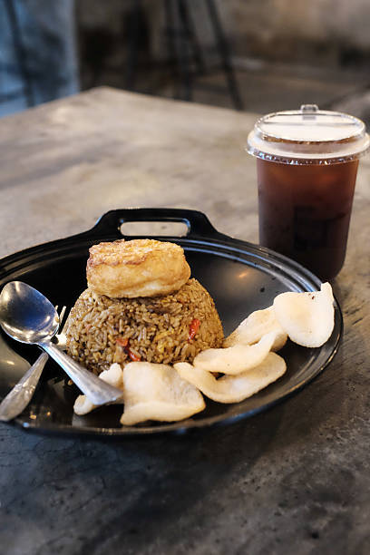 istock Delicious Asian fried rice served on a black tray with crispy crackers and fried tofu complemented by a cool beverage Asian culinary delight appetizing meal backdrop 2228729355