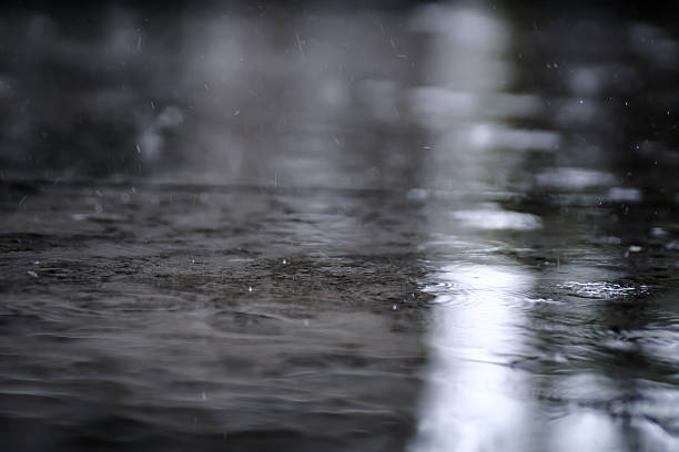 istock raining on the concrete walk way full with rain droplets splash ring bounce off the surface of water with reflected of white cloudy sky 2228732239