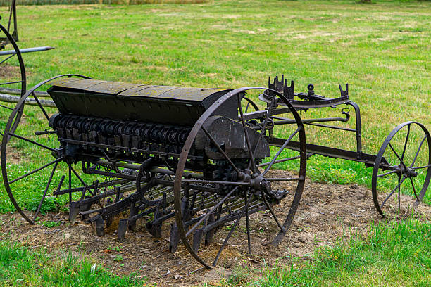 Vintage seed drill with cast iron wheels displayed on grass, formerly used in agriculture for sowing grain. Historic farming equipment as an outdoor exhibit.