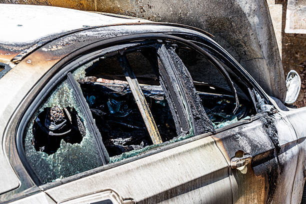 A car is in a junkyard with a wheel that is burnt and rusted. The car is surrounded by debris and the wheel is the only part of the car that is visible. Scene is one of destruction and decay