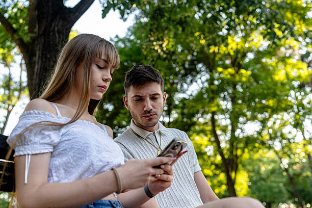istock Couple sitting on a park bench using a smartphone in a sunny setting 2228736700