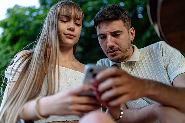 istock Young couple enjoying smartphone outdoors in a cheerful garden setting 2228736706
