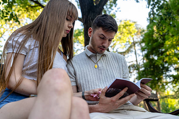 istock Young couple reading a book together on a park bench 2228737000