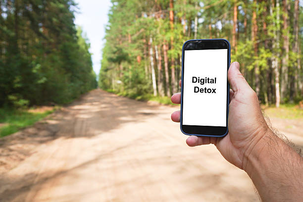 istock Man holding smartphone showing digital detox message in forest road 2228740971