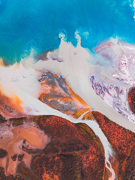 An abstract yet natural scene where flowing water meets vivid land, creating a striking aerial landscape.