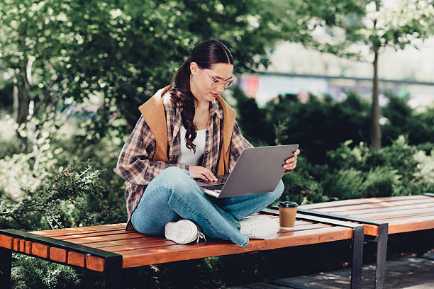 istock Young woman enjoying leisure time outdoors while working on laptop in casual style during a sunny day in the city 2228742757