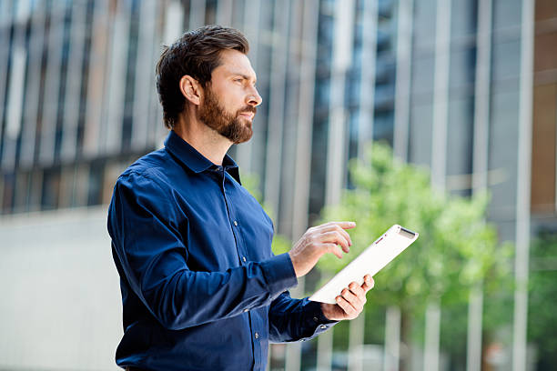 istock Elegant young businessman working with a tablet outdoors in a modern urban environment on a sunny day 2228744276